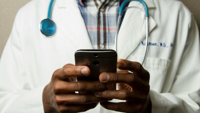 Doctor Holding Cell Phone. Cell phones and other kinds of mobile devices and communications technologies are of increasing importance in the delivery of health care. Photographer Daniel Sone